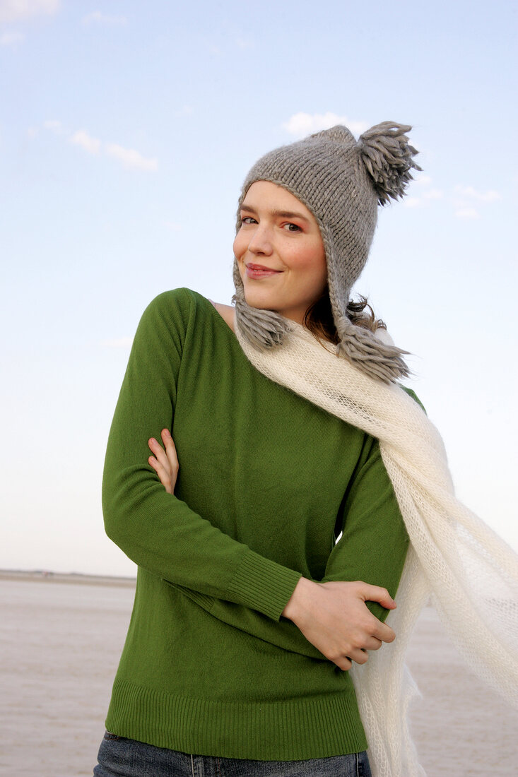 Beautiful woman wearing green sweater, jeans and scarf standing with arms crossed, smiling