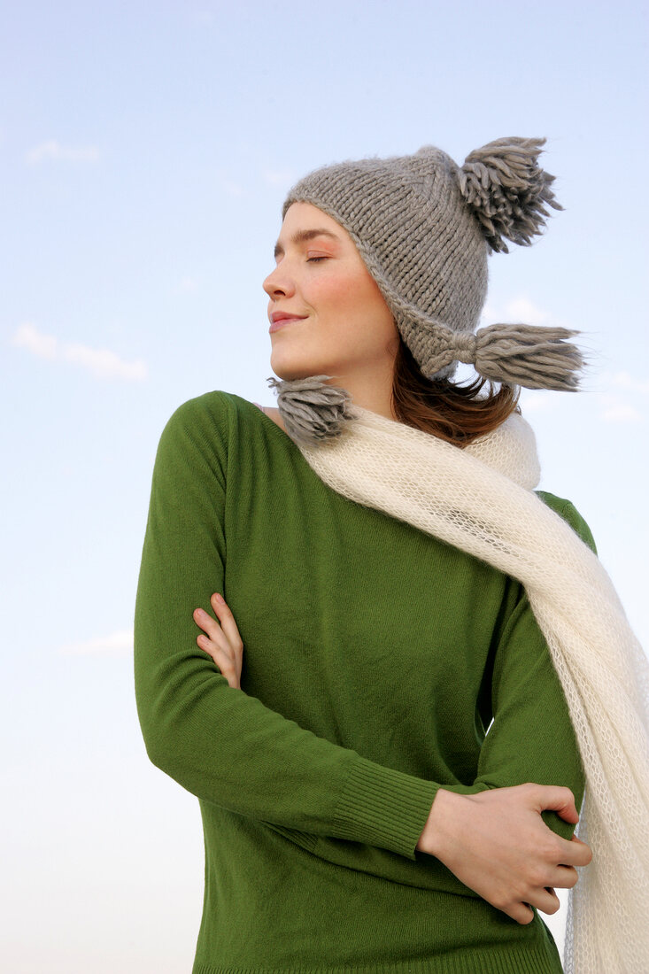 Beautiful woman wearing green sweater, jeans and scarf standing with arms crossed, smiling