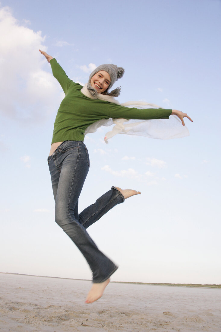 Beautiful woman wearing green sweater, jeans and cap jumping in air, smiling widely