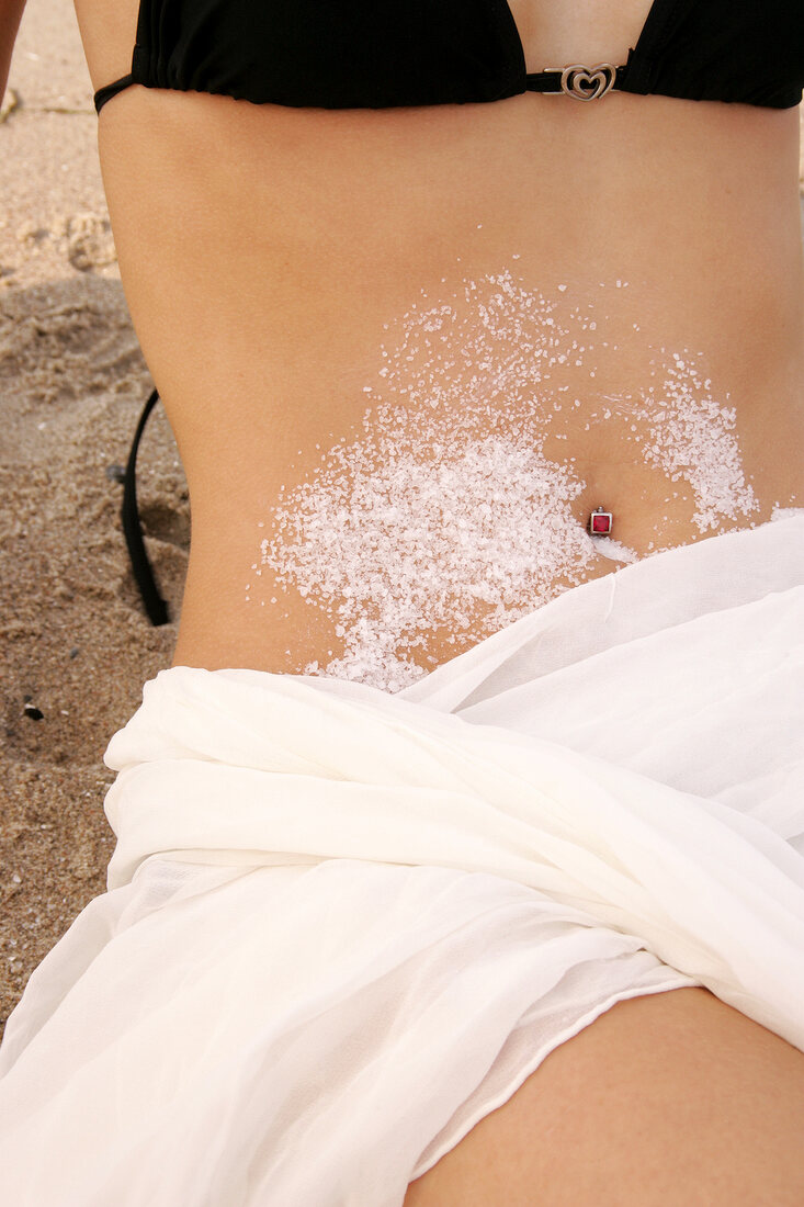 Frau liegt im Sand mit Salzkristallen auf dem Bauch