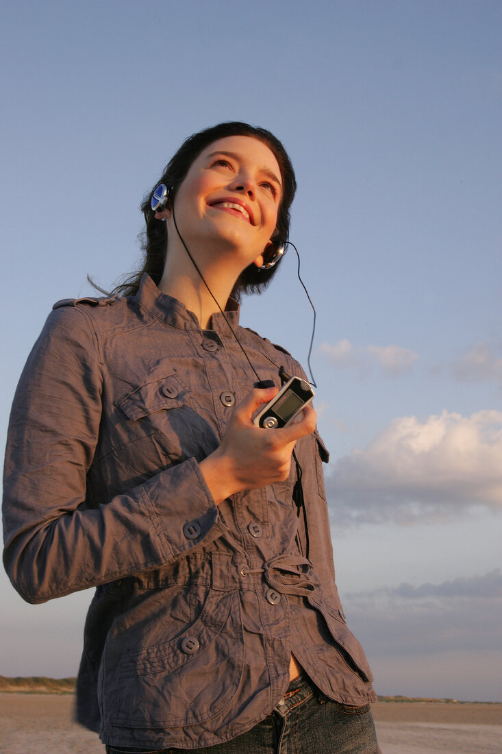 Pretty woman wearing brown shirt and jeans listening music, looking away and smiling