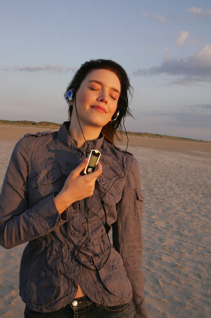 Pretty woman wearing brown shirt and jeans listening music, looking away and smiling