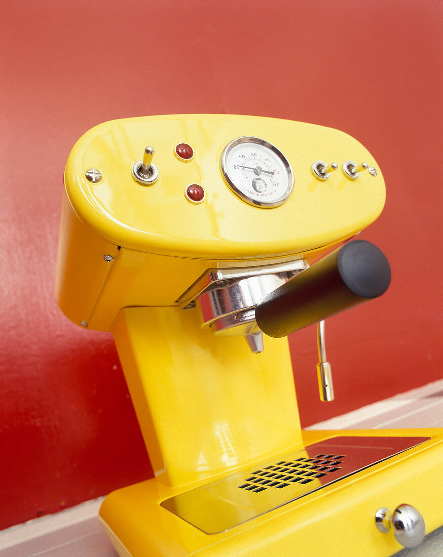 Espressomaschine aus gelb lackiertem Metall, Hintergrund rot