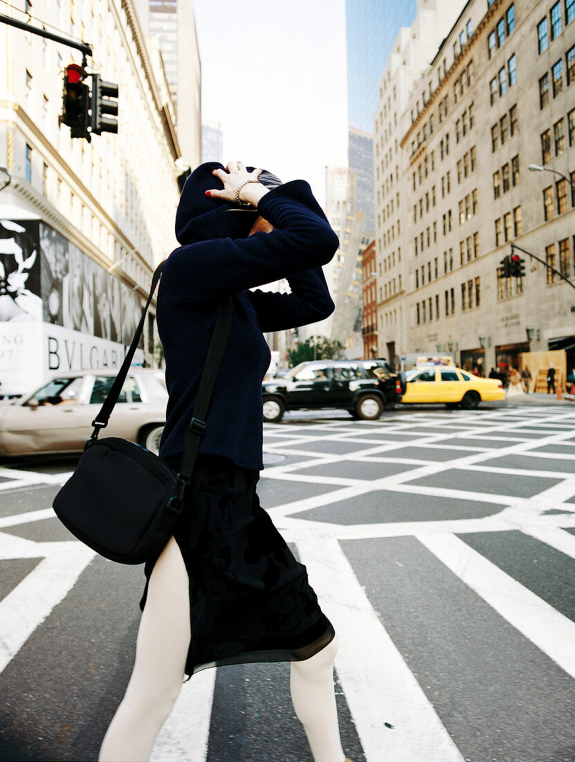 Side view of woman wearing black hooded jacket walking at zebra crossing