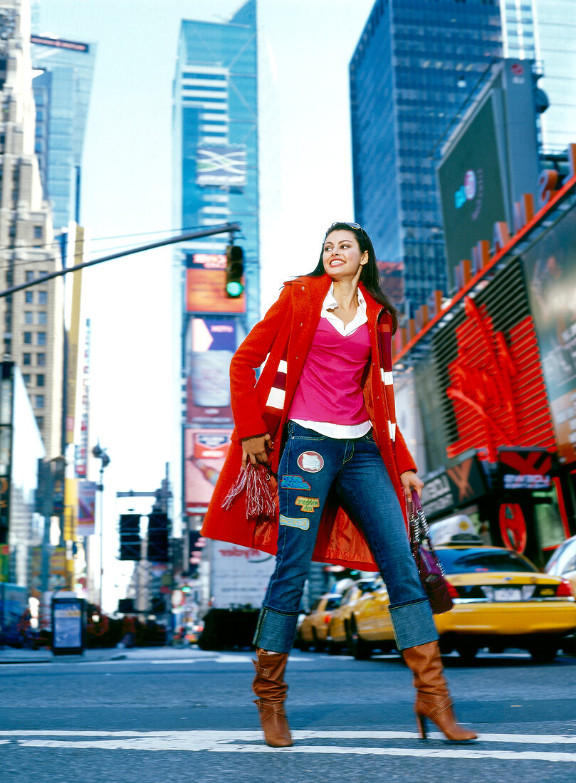 Happy woman wearing red coat, jeans and high-heeled boots walking merrily in New York, USA