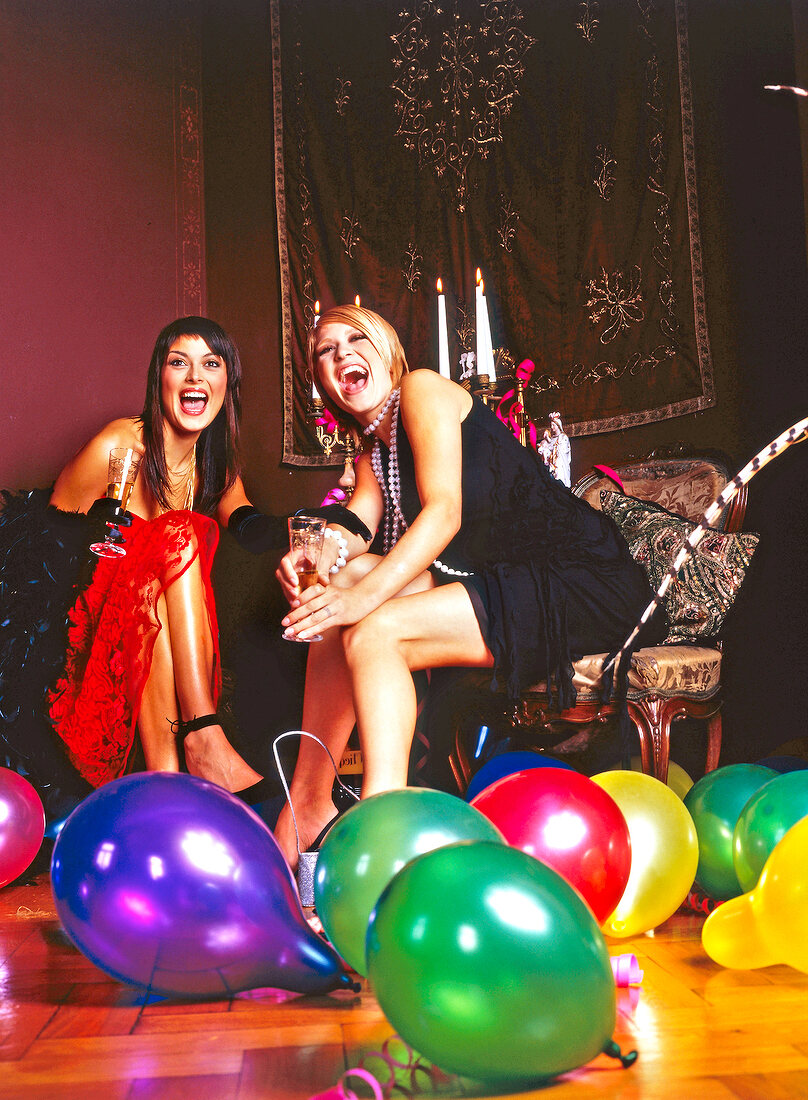 Cheerful women in dresses celebrating at party, surrounded with colourful balloons