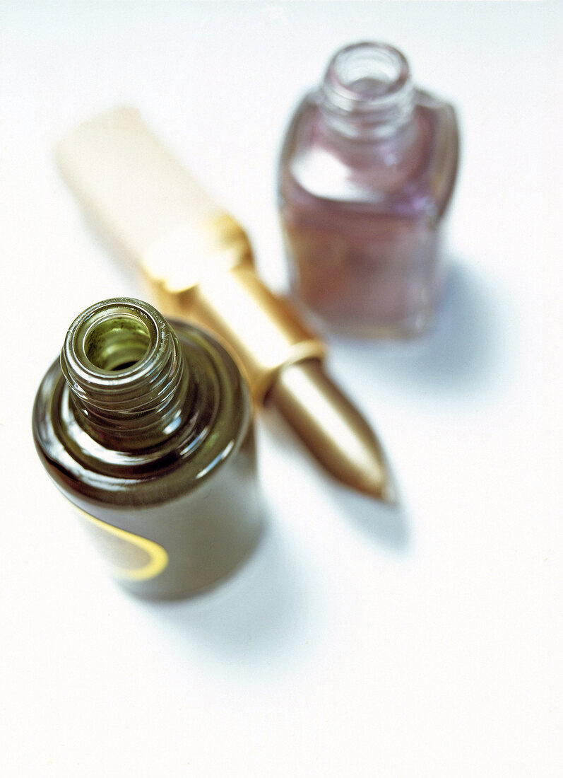 Close-up of nail polishes, lipstick in silver purple and silver green on white background