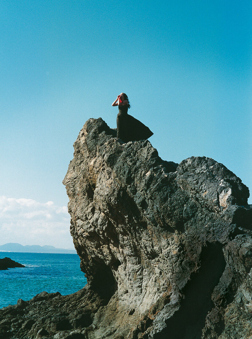 Woman standing on a cliff by the sea with both hands on the mouth as calling