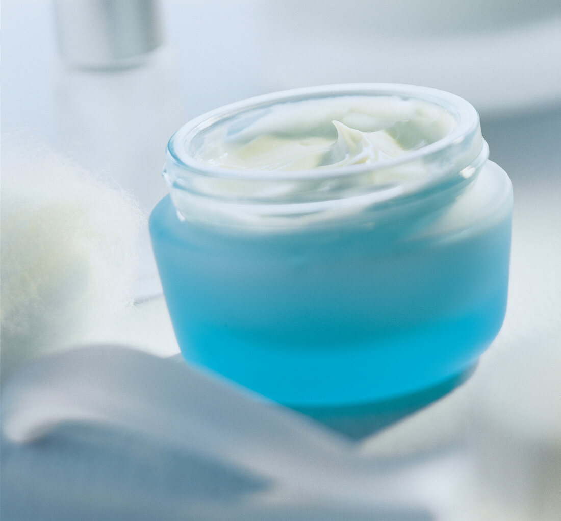 Close-up of glass with face cream in blue open container on white background
