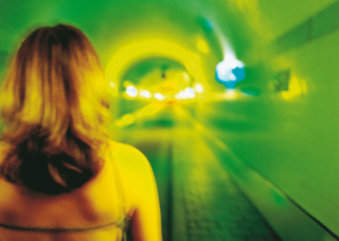 Rückansicht einer Frau, Blick in Tunnel, grelles Licht, Grün, Gelb