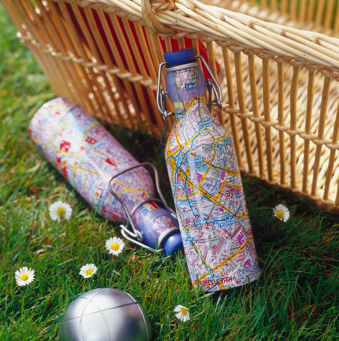 Two aluminium cylinders with map printings next to wicker basket on grass