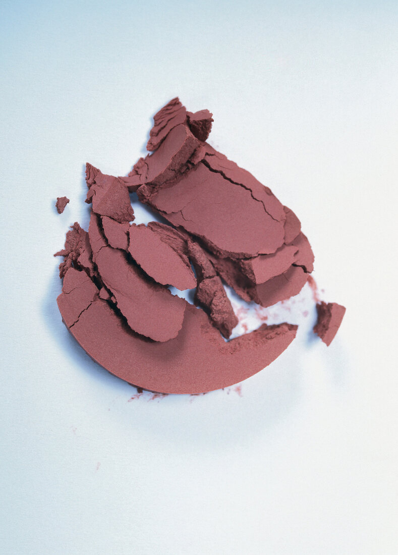 Close-up of crumbled pink silky shimmer blush on white background