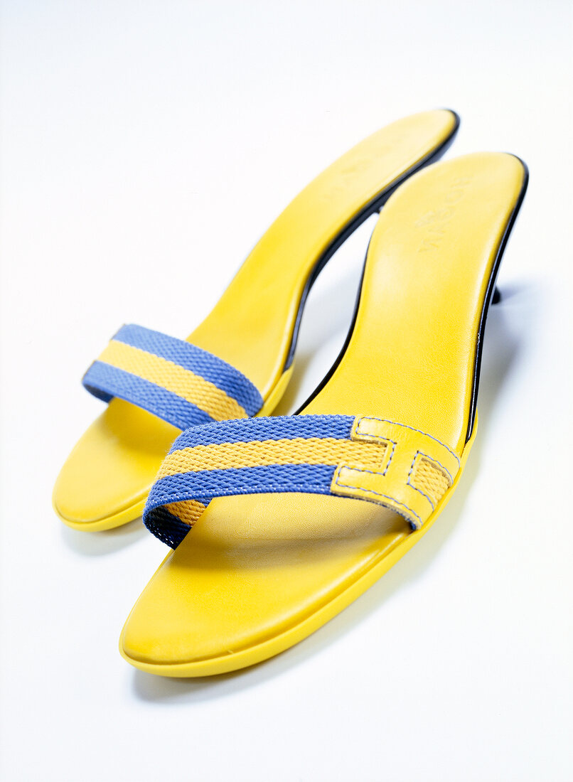Pair of yellow sandals with small heel and nylon strap on white background
