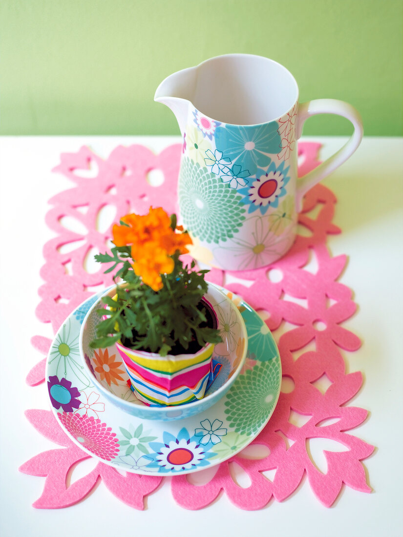 Jug, plate and bowl with flower on pink placemat, elevated view