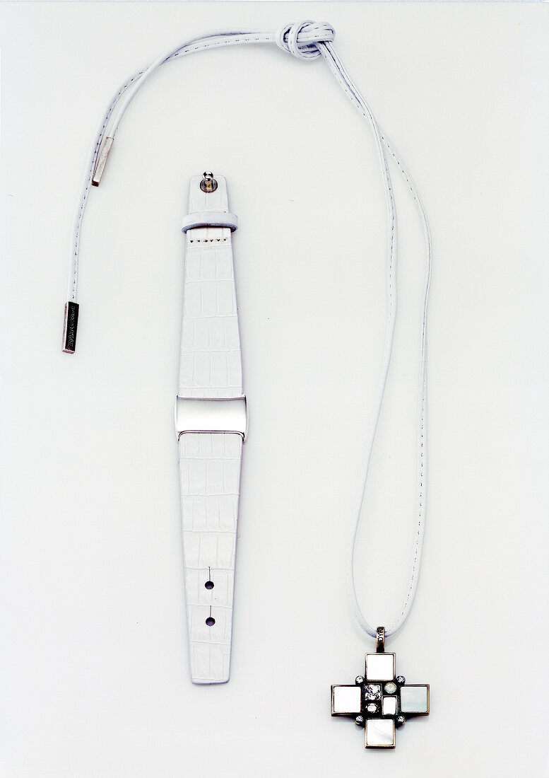 Close-up of leather hand band and silver necklace with cross on white background