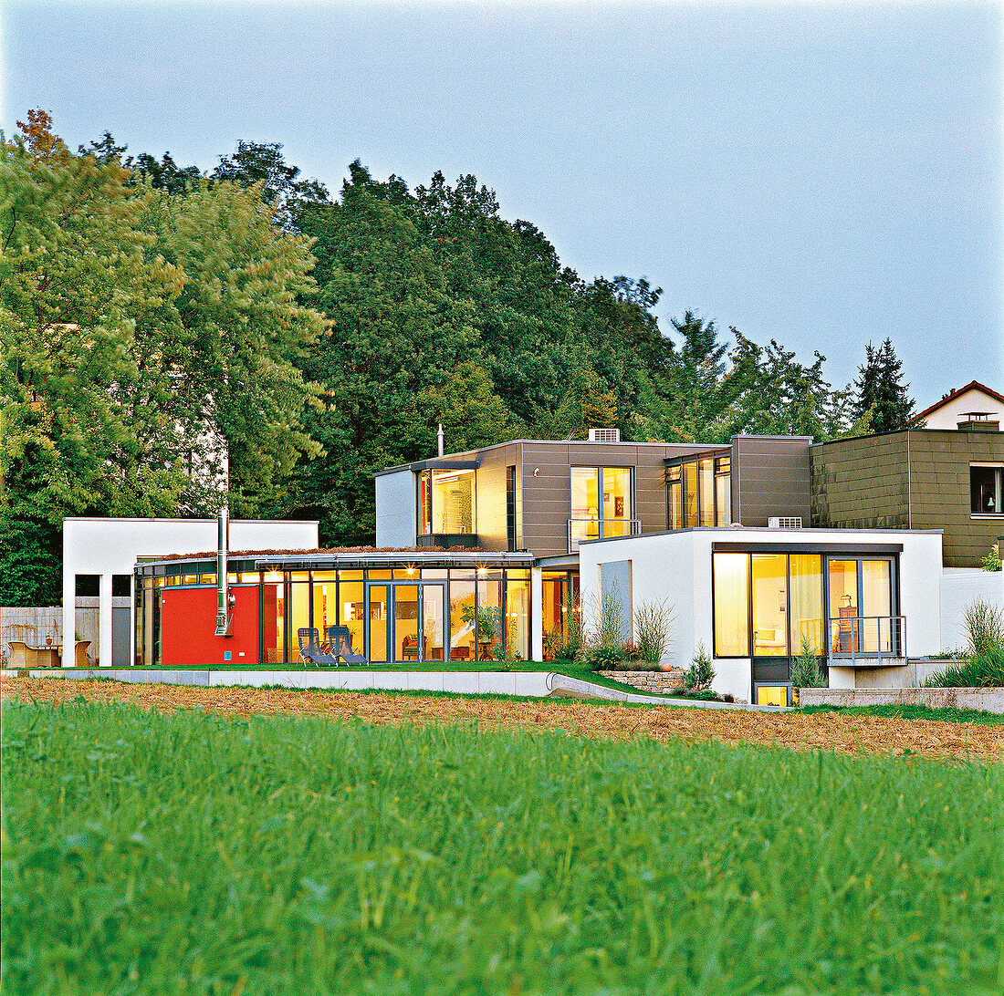 2 stöckiges Flachdachhaus mit vielen großen Fenstern, im Hintergr. Bäume