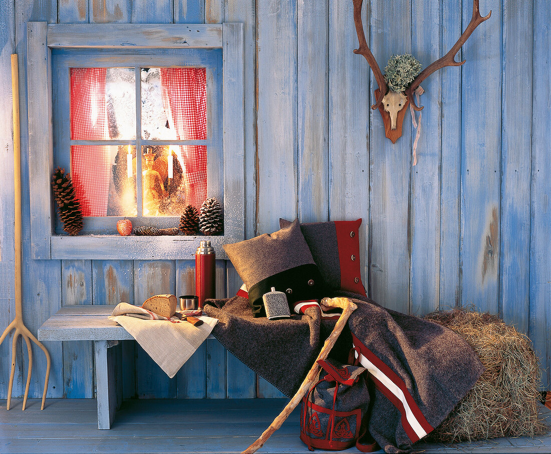 Bench seat with cushions on blue wooden wall in blue with illuminated window by side