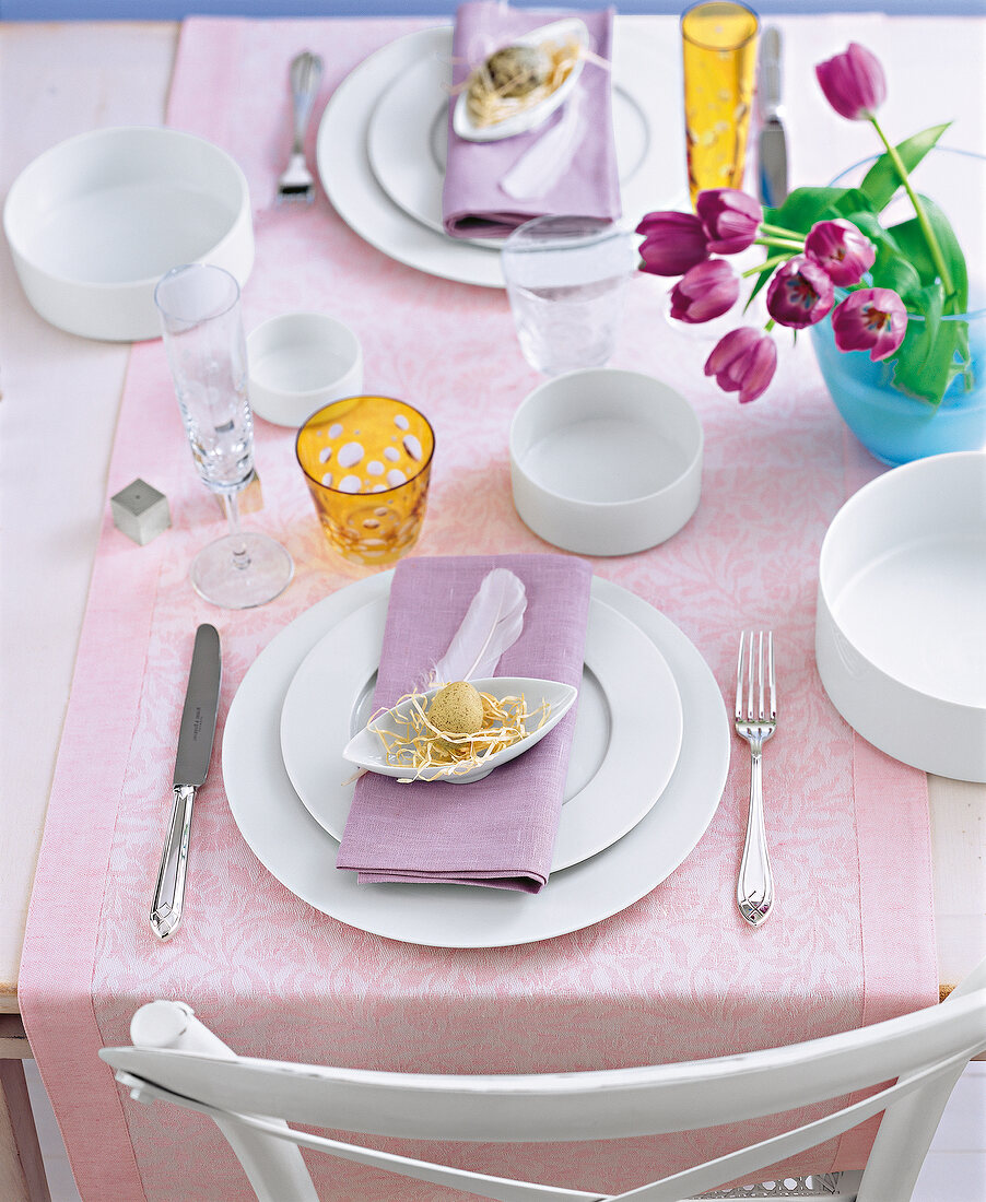 Quail egg in oval shell, white crockery and tulip in glass vase on table