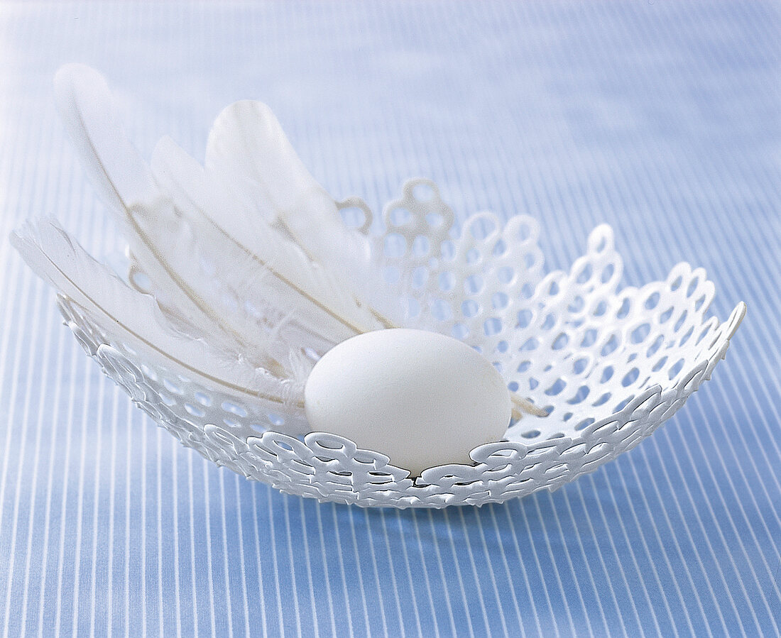 weiße, handgefertigte Schale, darin liegen Federn und ein Ei