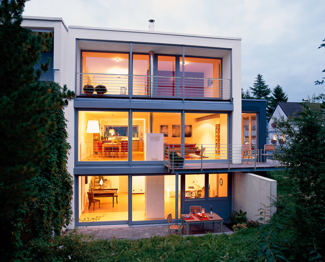 Exterior of illuminated house with three floors and large glass windows