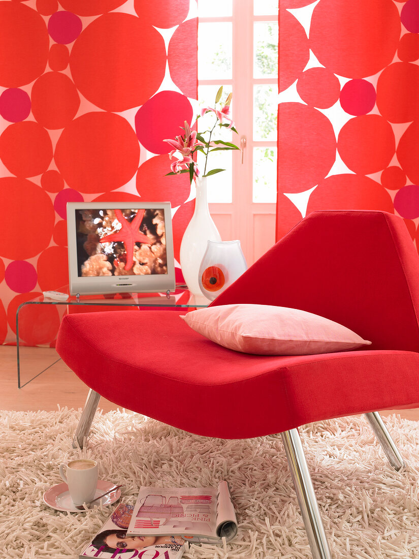 Close-up of red chair with cushion in front of red dotted curtains