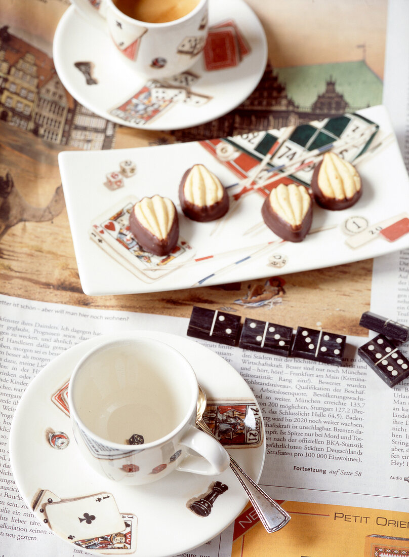 Two coffee cups on newspaper with triangle shape chocolates on plate
