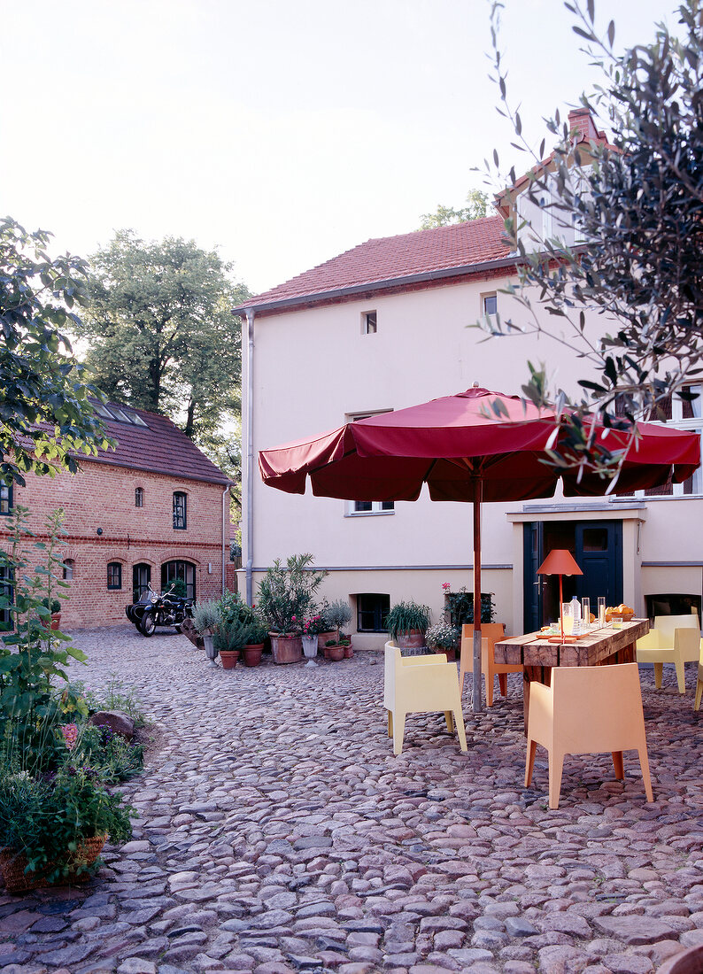 Exterior of building with paved patio and table with chairs under red parasol