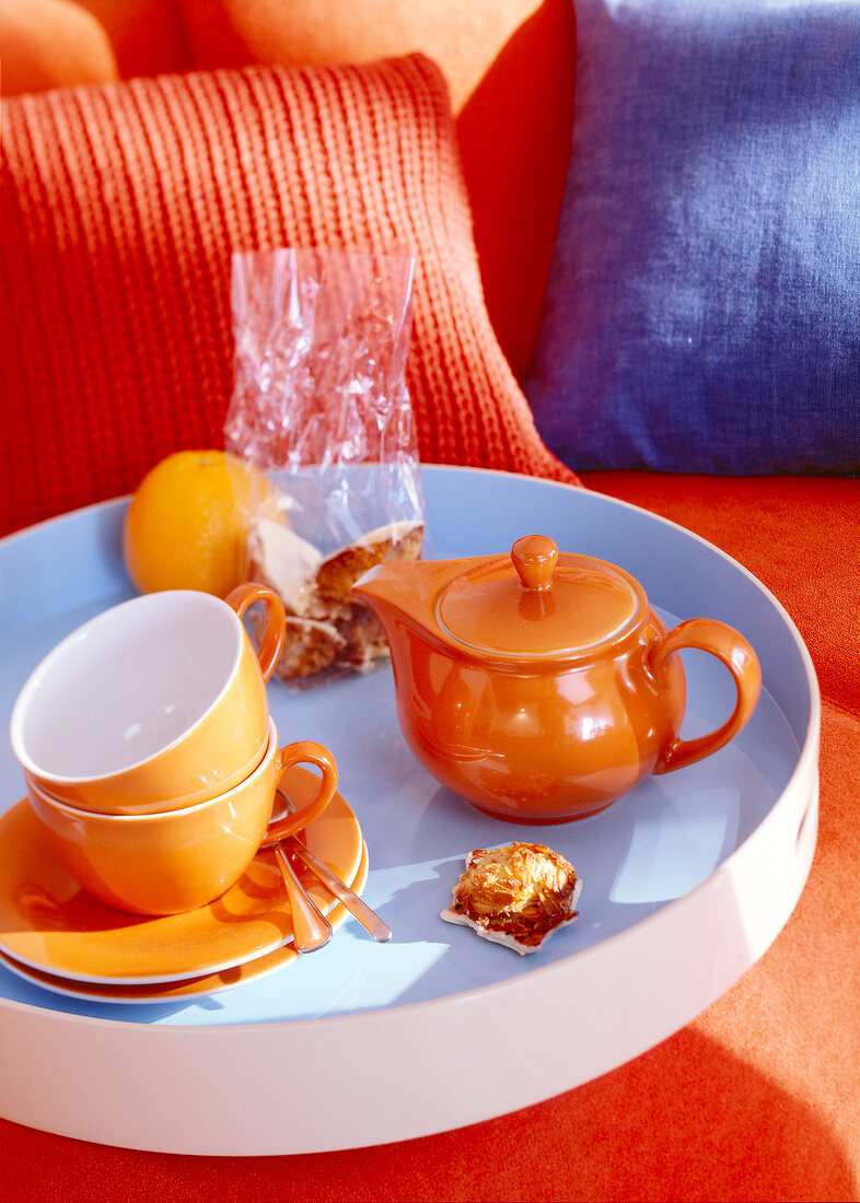 Tablett mit orangenem Geschirr steht auf einem Sofa.