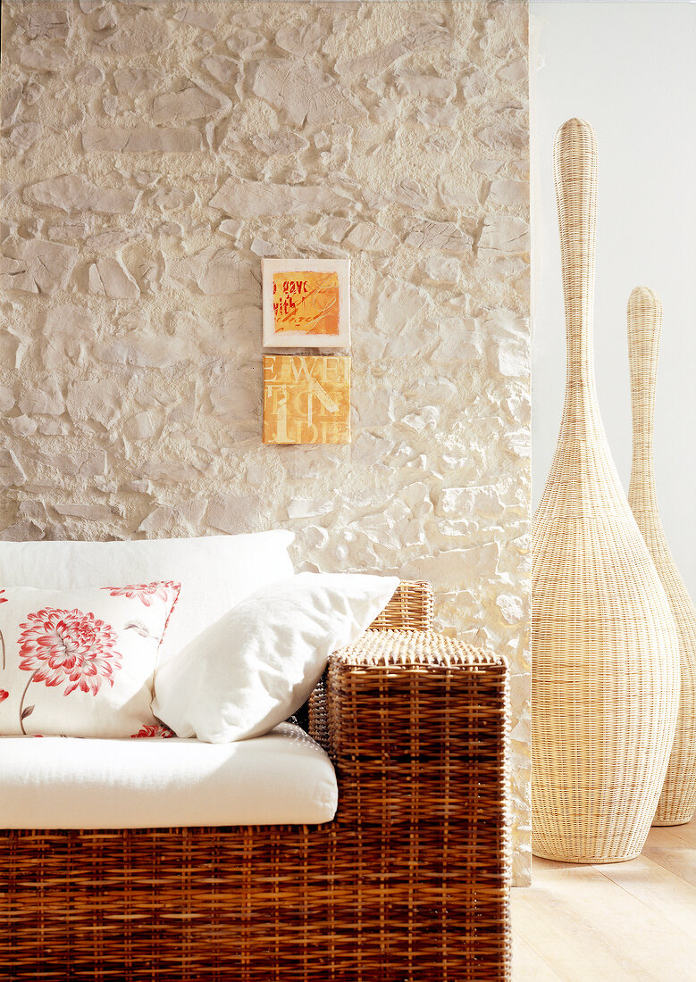 Rattan sofa with cushions against light coloured stone wall
