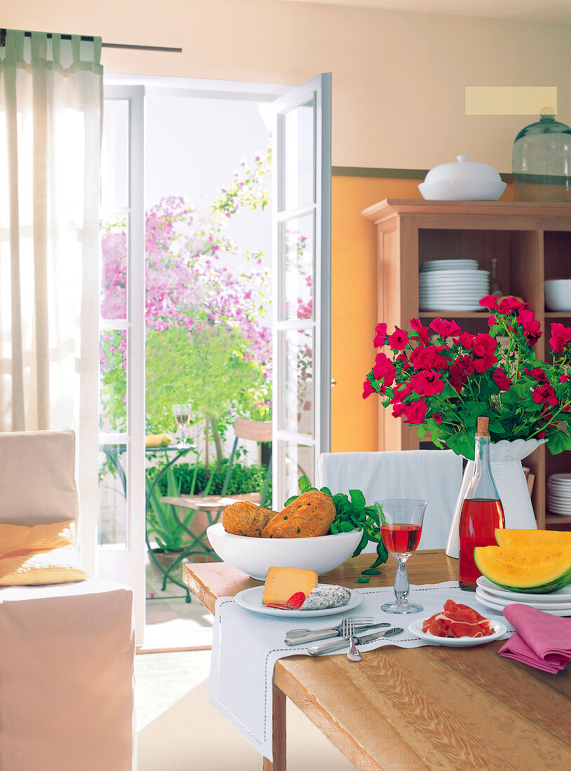 Set table with flowers in white vase in front of open patio door