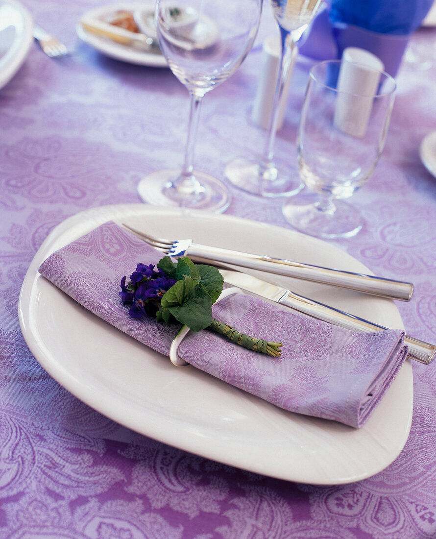Pastel coloured napkin decorated with bunch of small violets and cutlery on plate