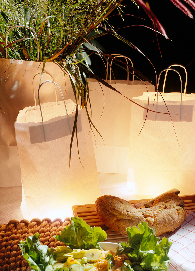 3 braune Papiertüten-Lampen, Salat, Brot und ein Strauß mit Gräsern.