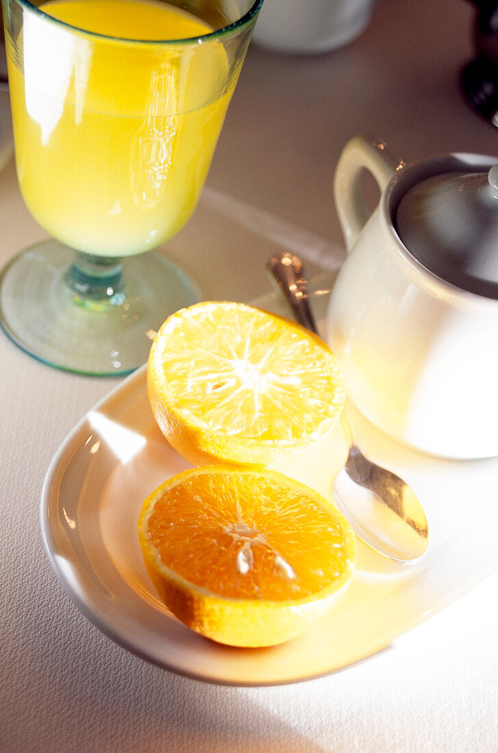 Orange halbiert auf Teller + Glas Orangensaft, Nahaufnahme