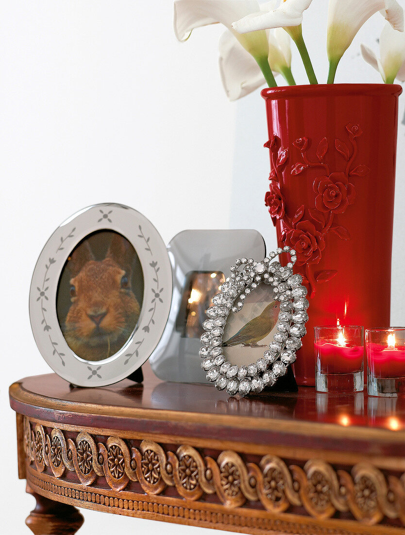 Close-up of opulent picture frame, lit glass candles and red vase on console table
