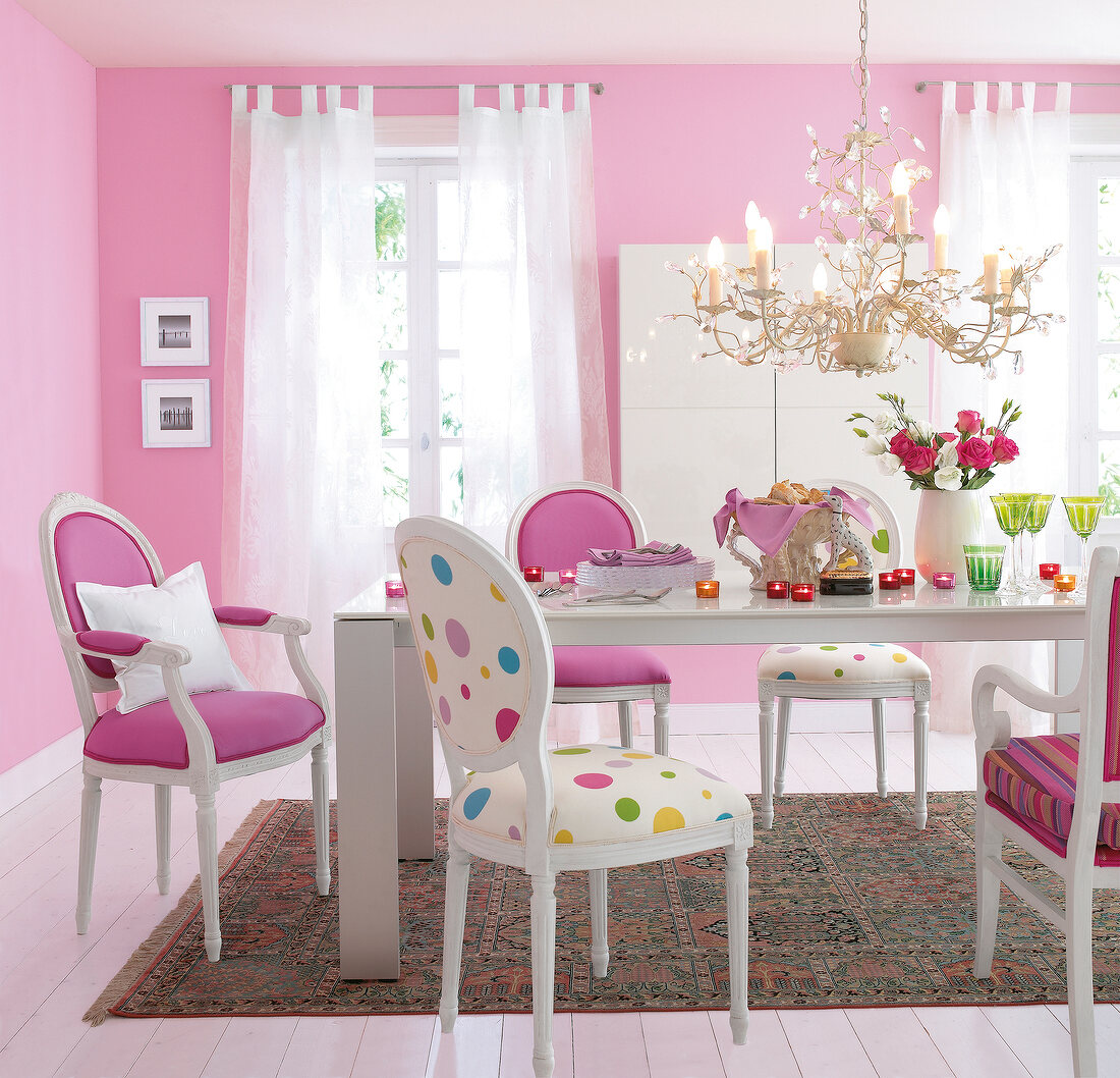 Dining room with pink walls, glass top table, multi-coloured chairs and chandelier