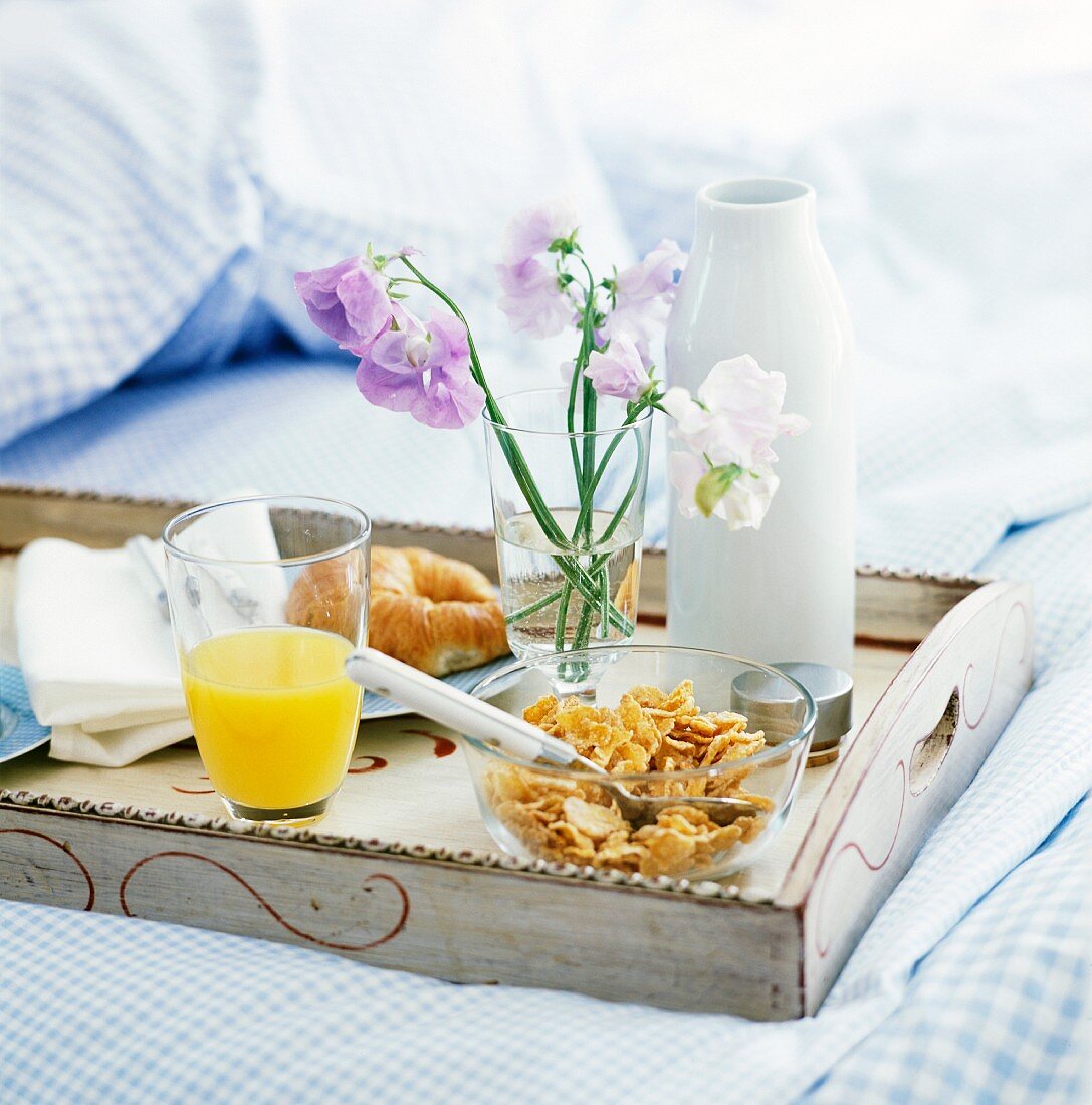 A croissant, cornflakes and orange juice on a breakfast tray