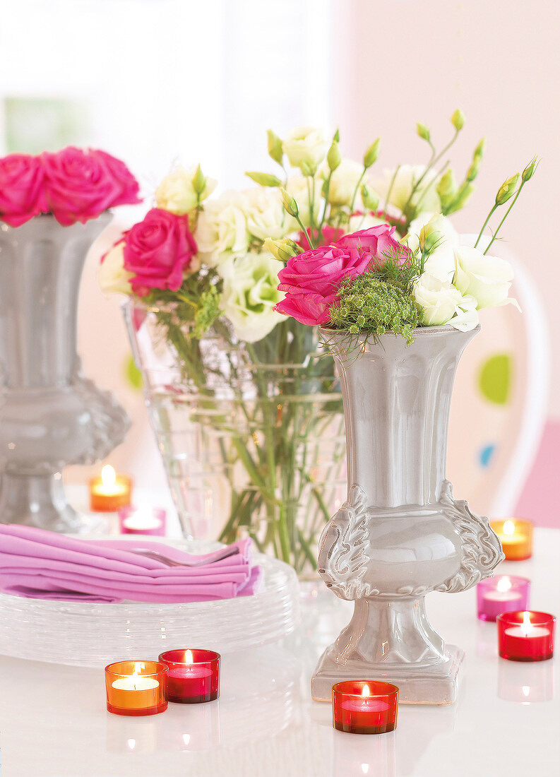 Table decoration with white and pink roses in ceramic vases and lit glass candles