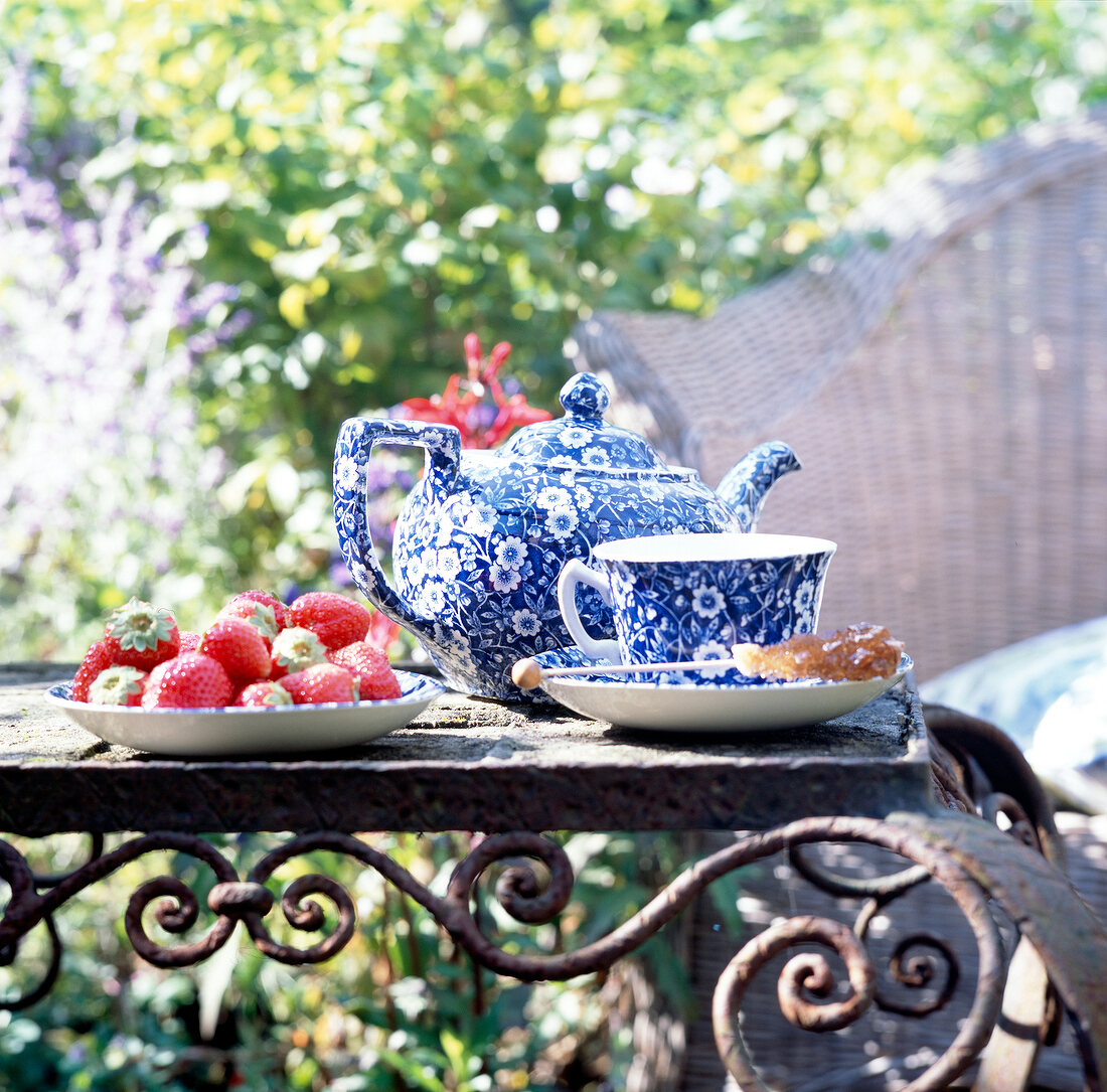 Blaue, geblümte Teetasse u. Kanne, Teller m. Erdbeeren auf e. Tisch.