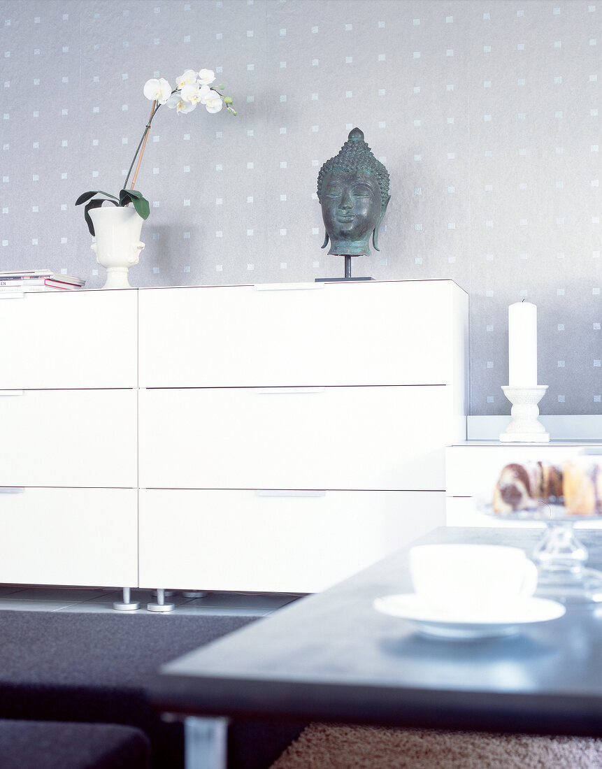 White chest of drawers in living room with orchids in vase and Buddha statue