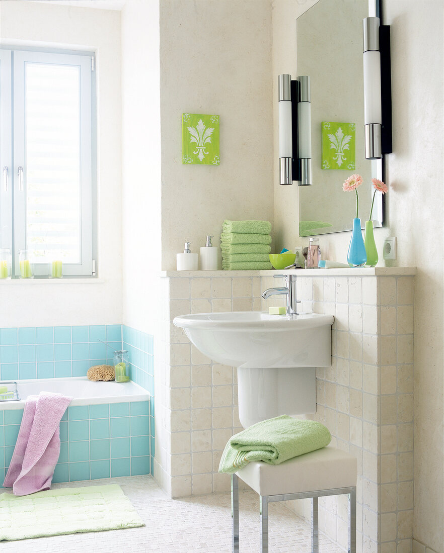 Bathroom with white and light blue tiles, green towels, sink and bathtub