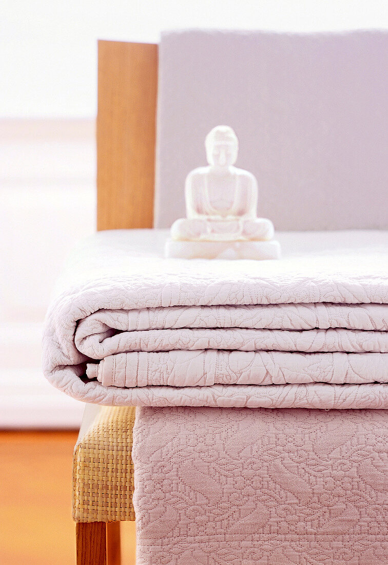 Sculpture of Buddha with white quilt on chair