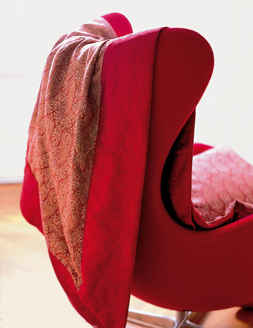 Decke mit floralem Motiv und rotem Rand, über der Sessellehne.
