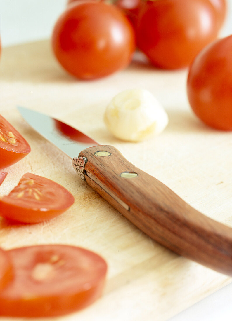 Close-up of chopped cherry tomatoes with garlic clove and knife on chopping board