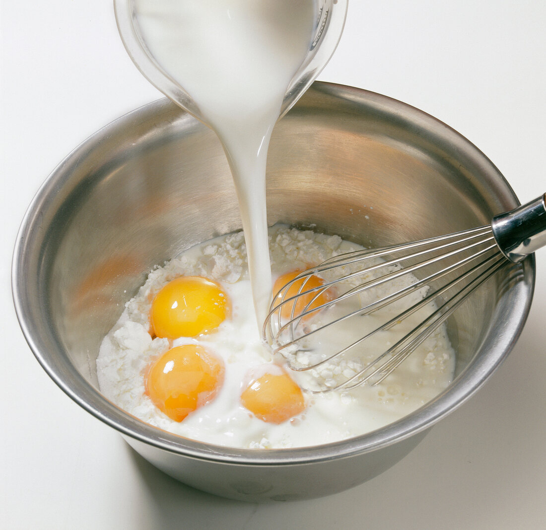 Milk being poured in mixture of flour, egg yolks and sugar in bowl