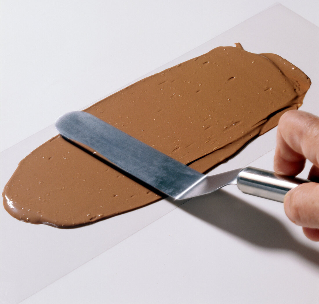 Hand spreading melted chocolate with spatula on baking paper