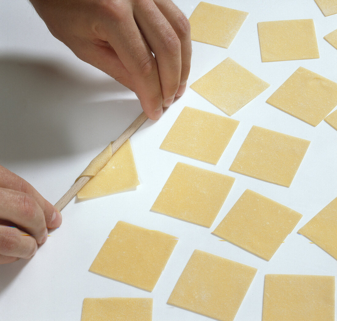 Hand wrapping square shaped dough on round timber for preparing garganelli pasta, step 1