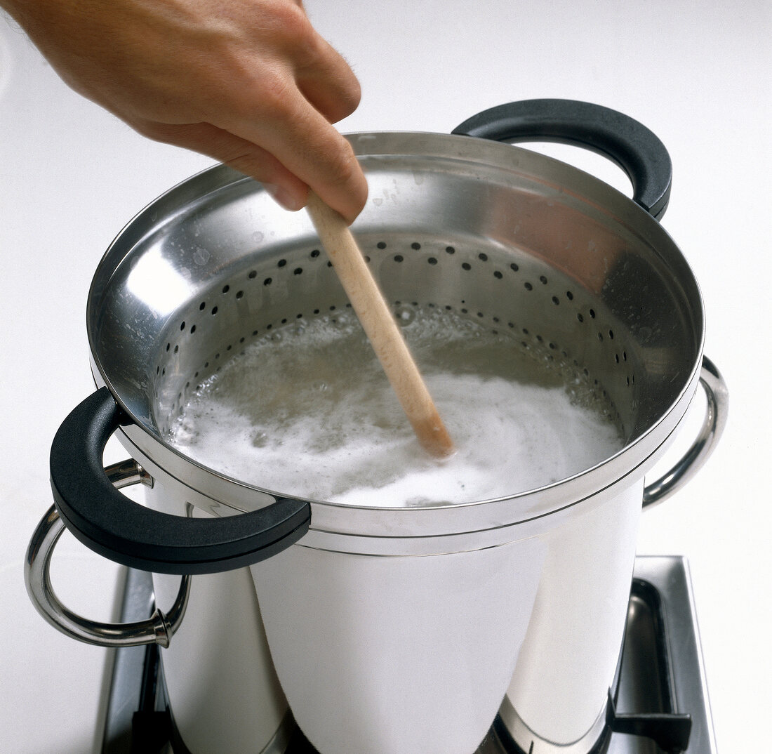 Hand stirring noodles in strainer for preparing pasta, step 2