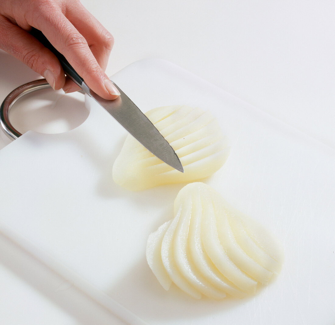 Peeled and halved pear being cut into slices on cutting board