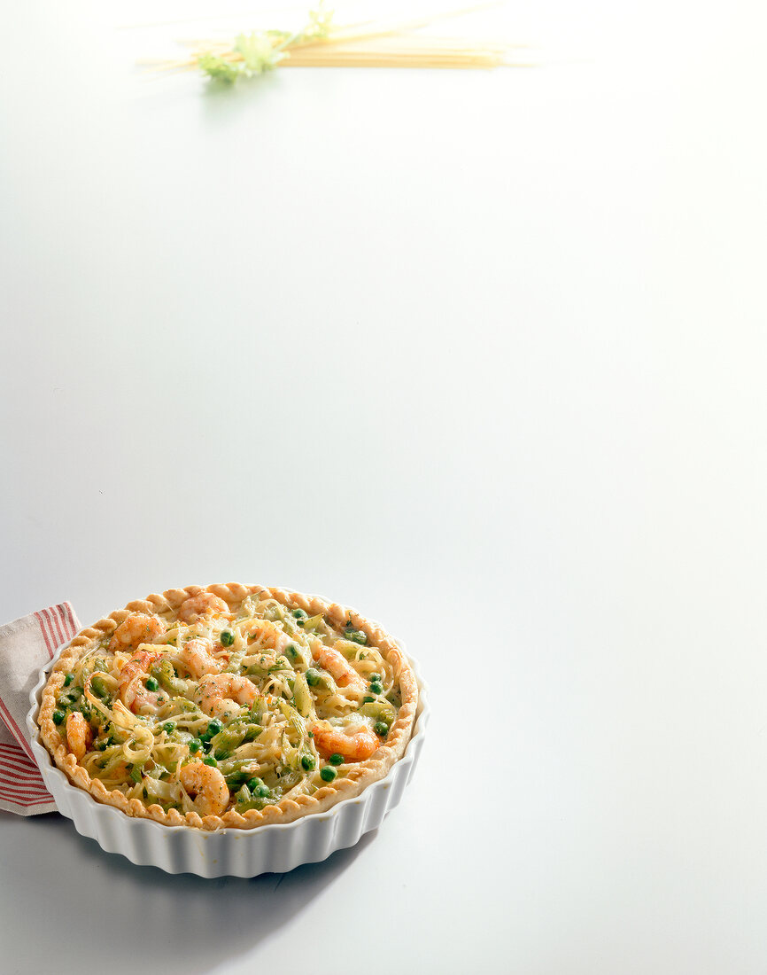 Spaghetti pie with shrimp and vegetables in baking dish on white background