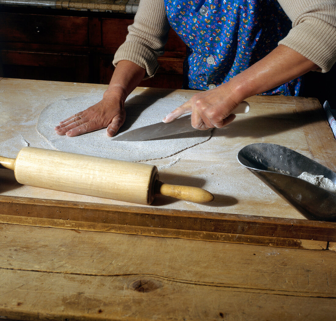 Woman cutting rolled buckwheat dough with knife on table, step 4